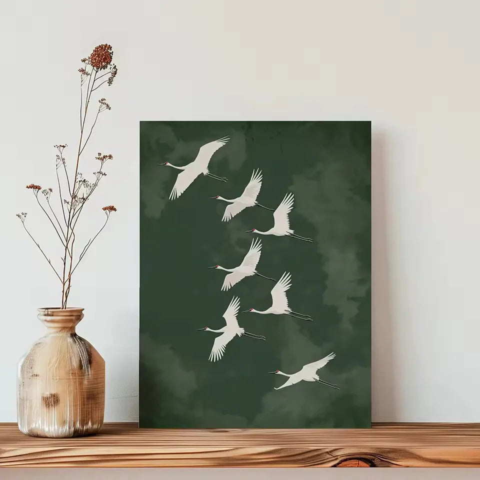 Framed artwork of cranes on a green background next to a vase with dried flowers.