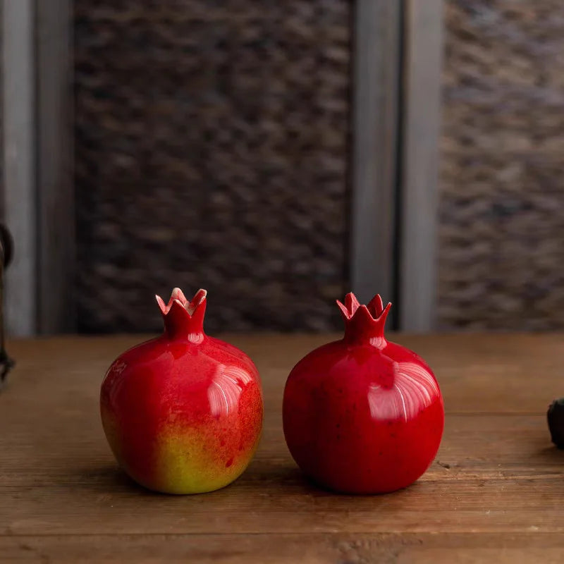 Two red ceramic pomegranates on a wooden surface with a blurred background