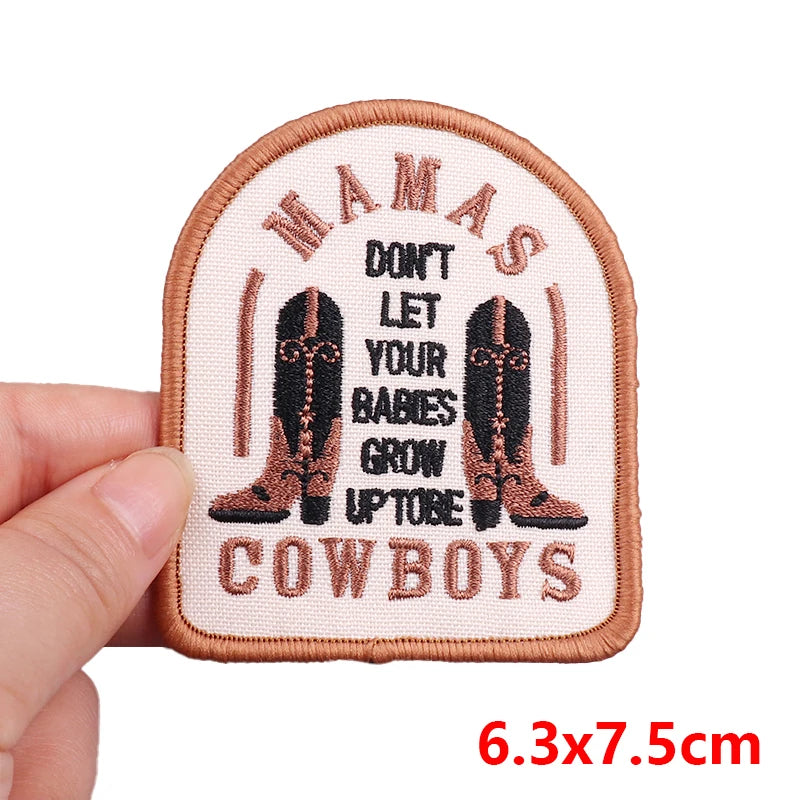 Embroidered patch with cowboy boots and text held by a hand, on a white background.