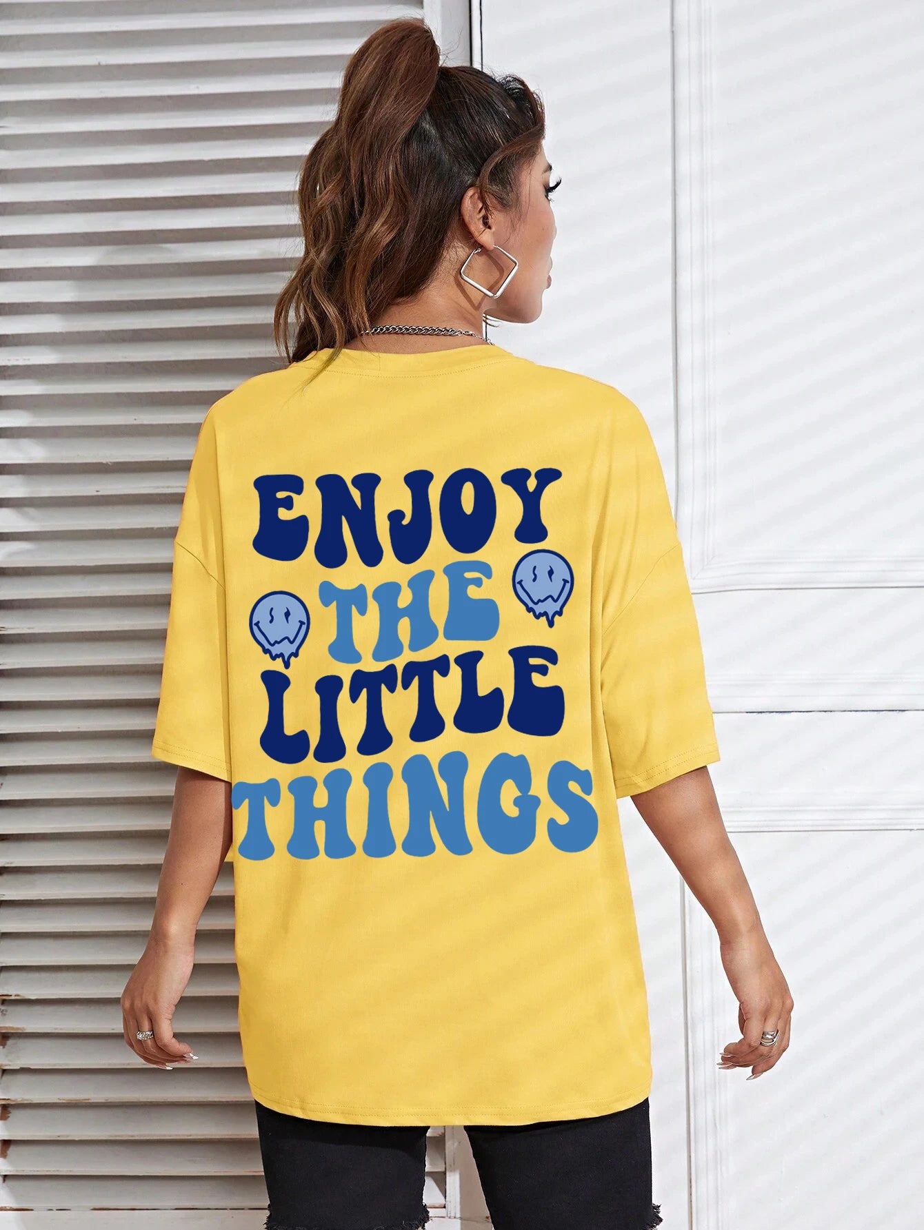 Person wearing a yellow t-shirt with 'Enjoy the Little Things' text and smiley face symbols.