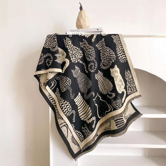 A black woven throw blanket with cream-colored cat and tree patterns, draped over a white shelf with a decorative pear hanger.