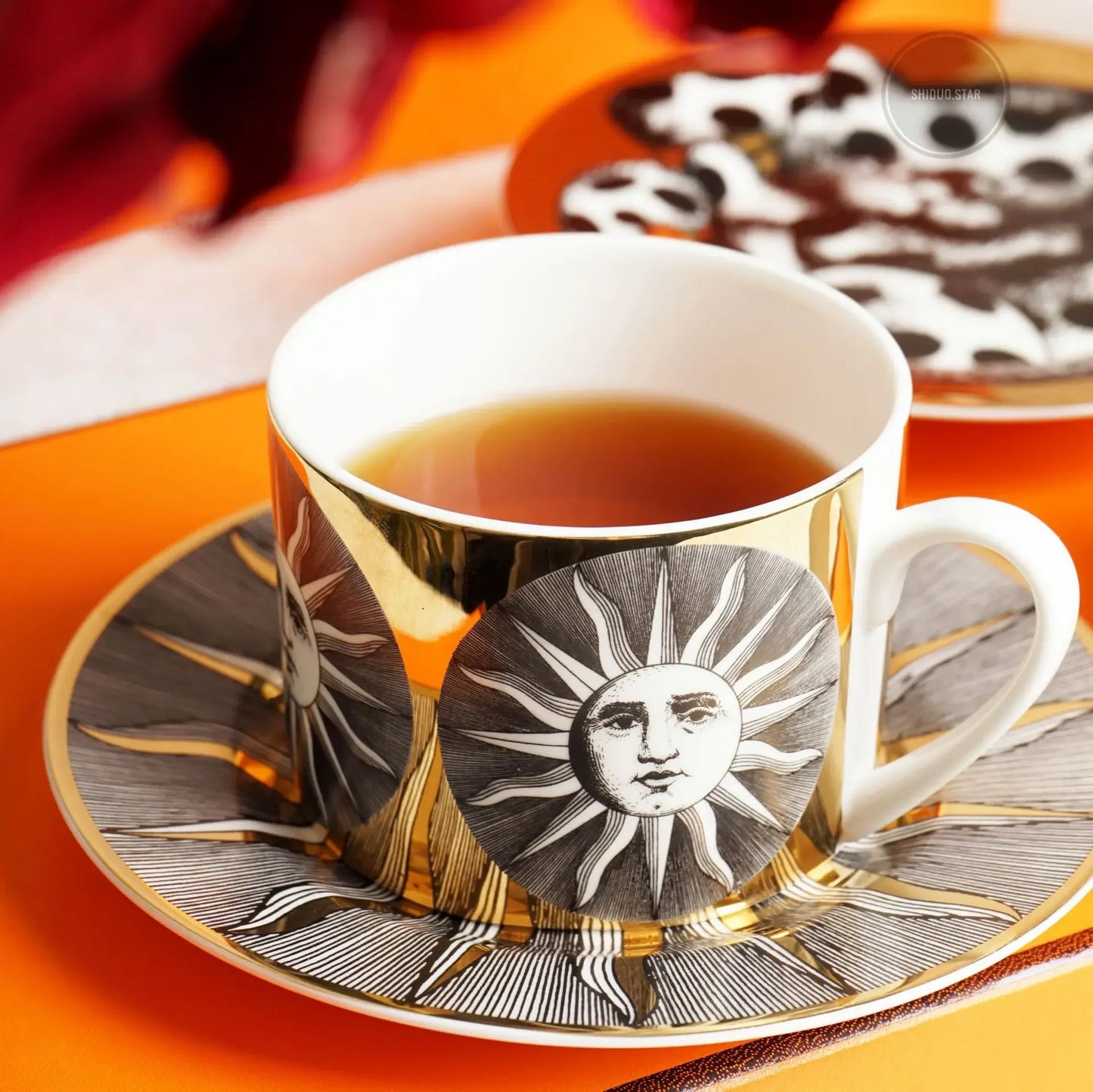 Decorative tea cup with sun design on a matching saucer on an orange surface.