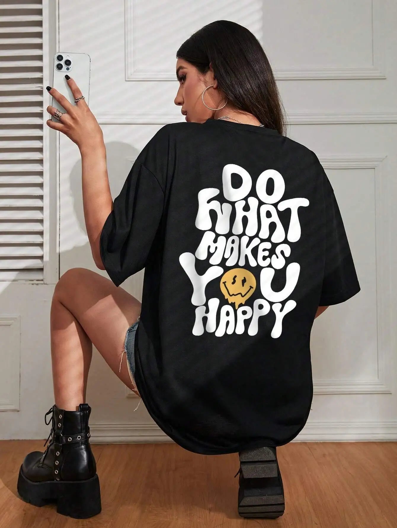Person wearing a black oversized t-shirt with a motivational quote on the back, sitting against a white wall.