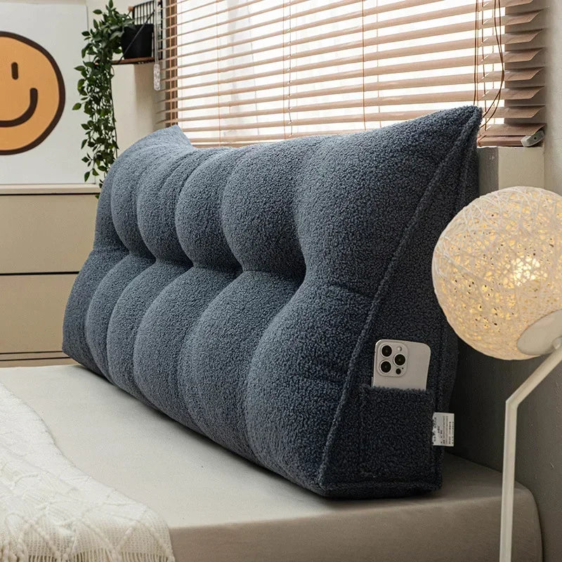 Gray wedge pillow on a bed with a smiley face decoration in the background
