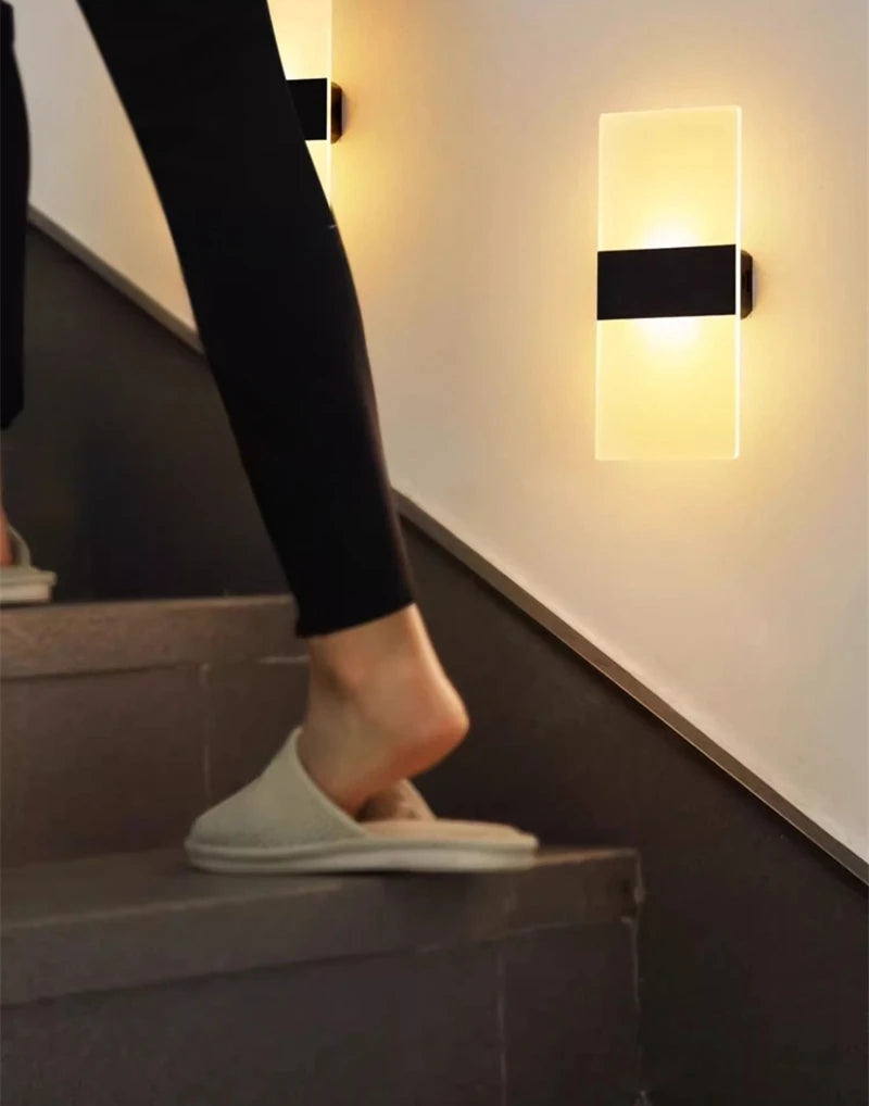 Person walking up a staircase with a wall light fixture on the wall.