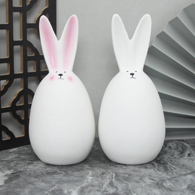 Two white rabbit-shaped night lights on a gray surface with a decorative background.