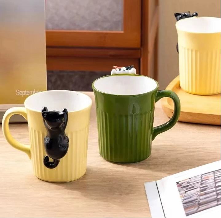Green and yellow ceramic cat mugs with a 3D cat climbing over the rim.