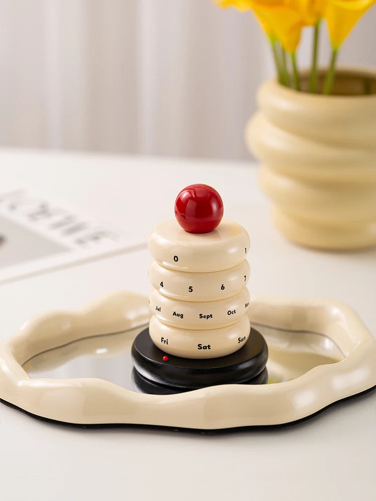 Decorative calendar shaped like a cake with a cherry on top, placed on a white surface.