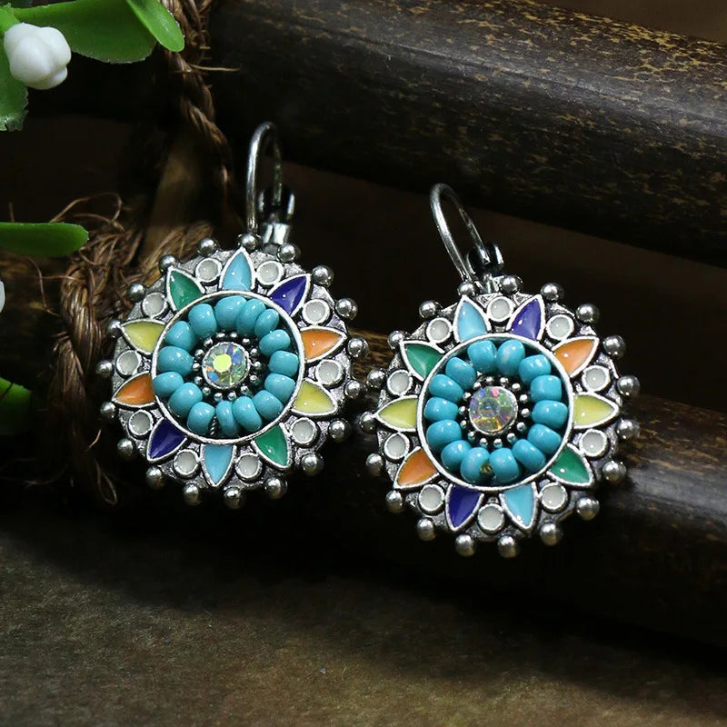 Pair of decorative earrings with turquoise and multicolor design on a dark surface.