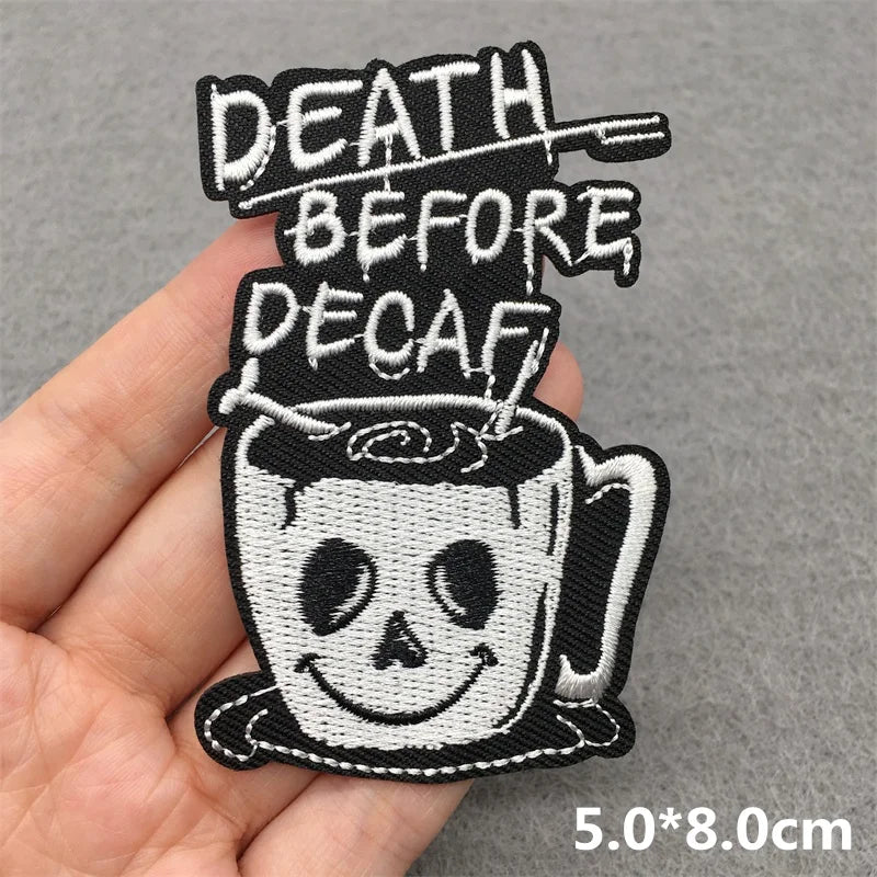 Embroidered patch with 'Death Before Decaf' text held by a hand on a gray background