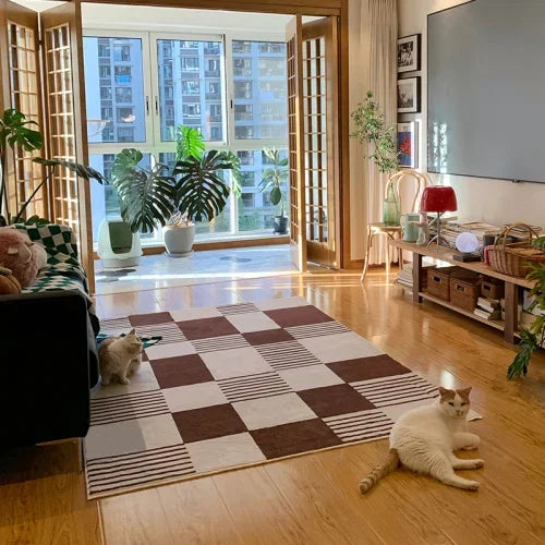 Living room with a checkered rug, cats, and a large window.