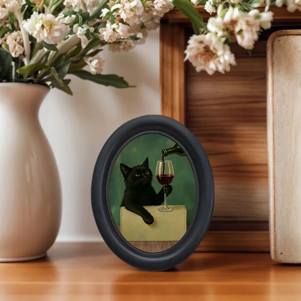 Decorative item with a black cat holding a glass of red wine, placed on a wooden surface with flowers in the background.