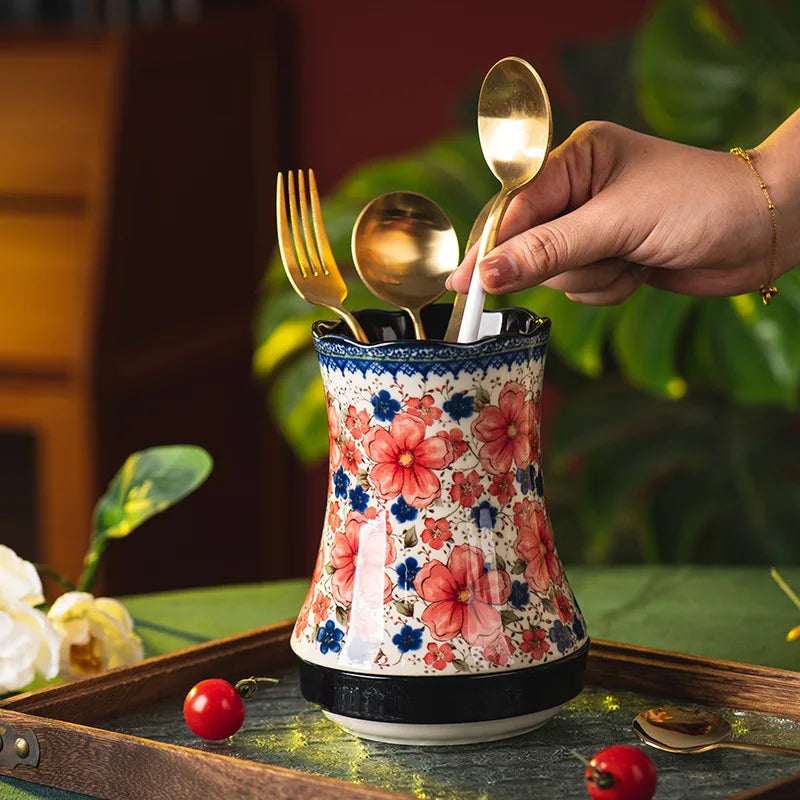 Floral-patterned cutlery holder with gold fork, spoon, and knife on a table.