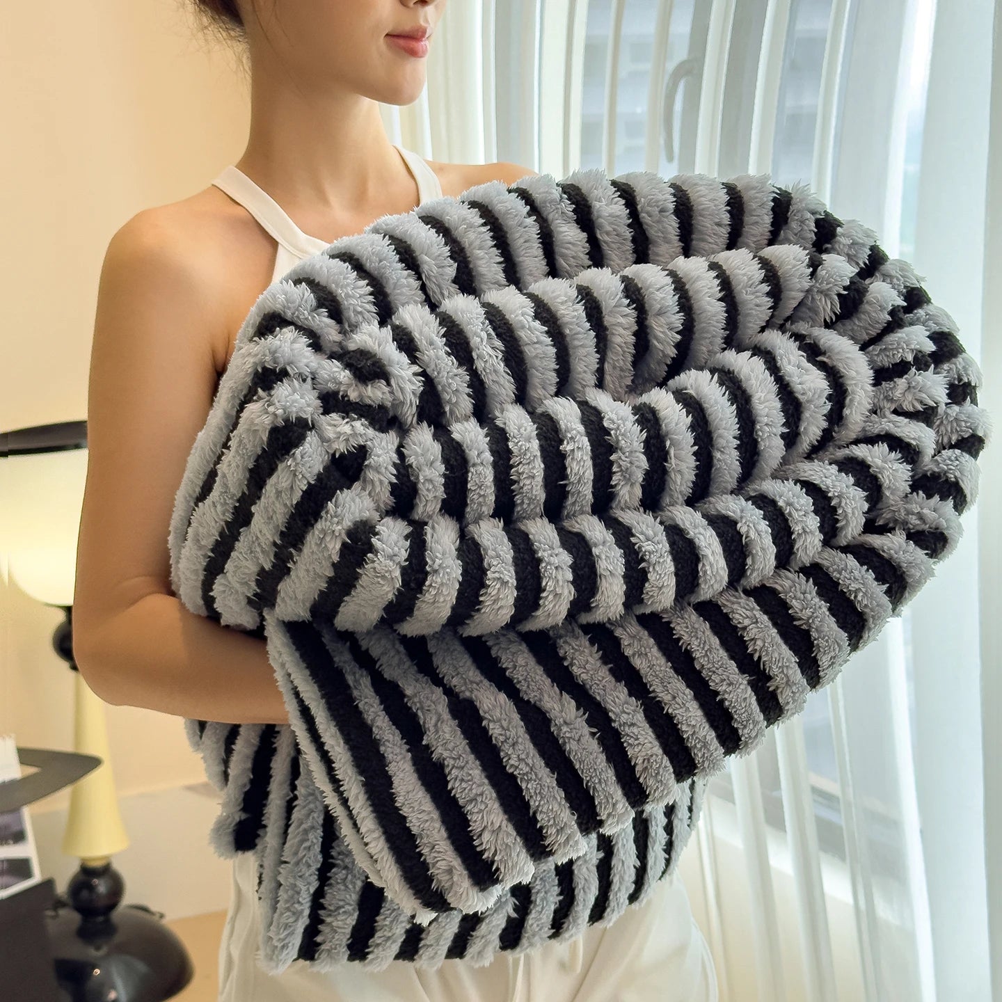 Person holding a striped gray and black blanket indoors