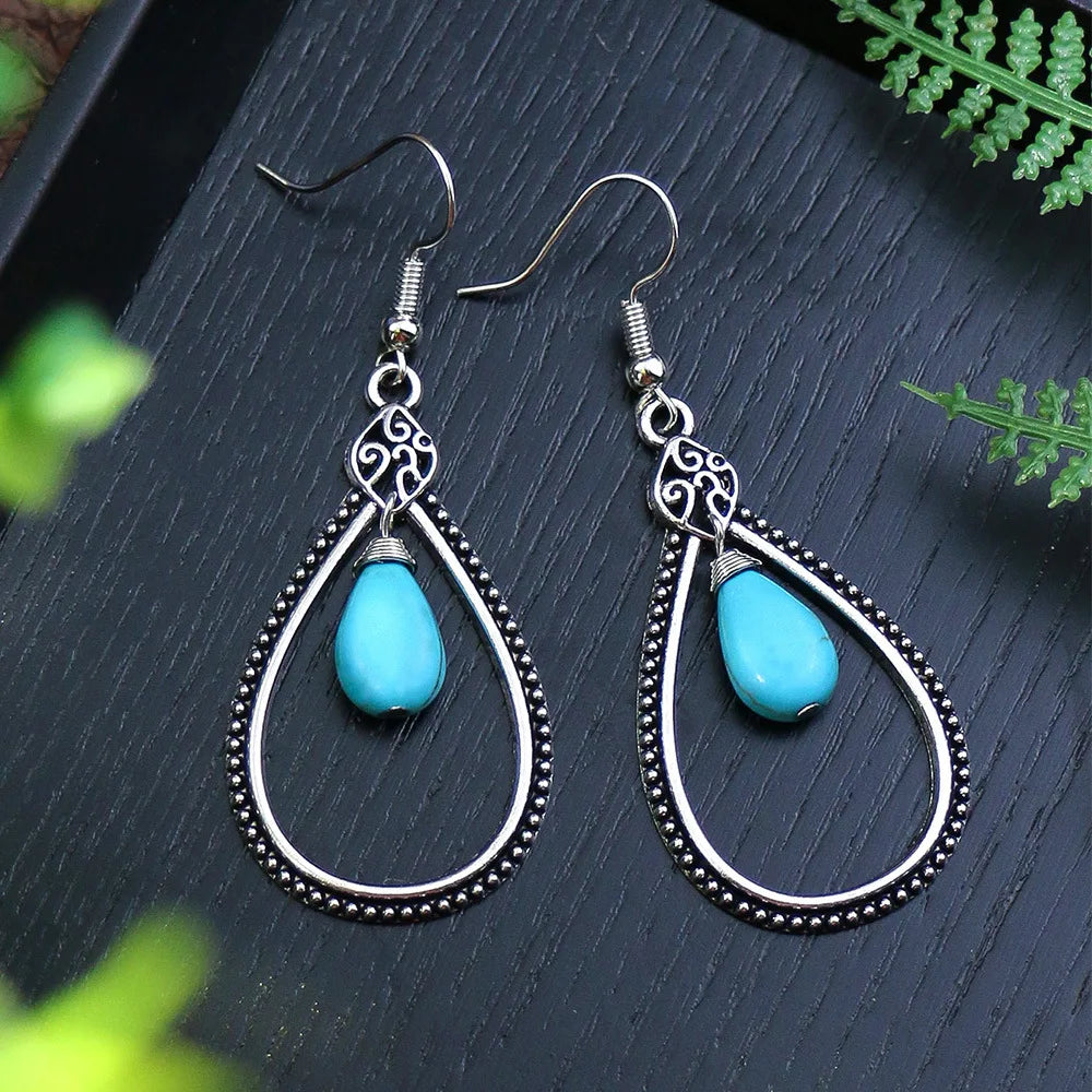 Teardrop-shaped earrings with turquoise stones on a dark surface