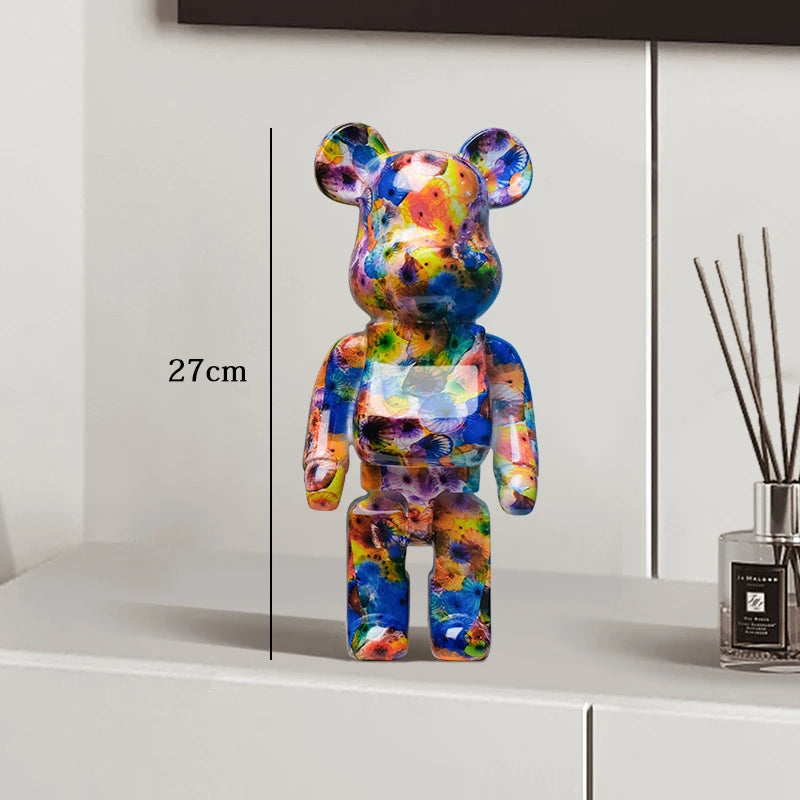 Colorful bear-shaped figure on a white surface with a measurement label, next to a diffuser bottle.