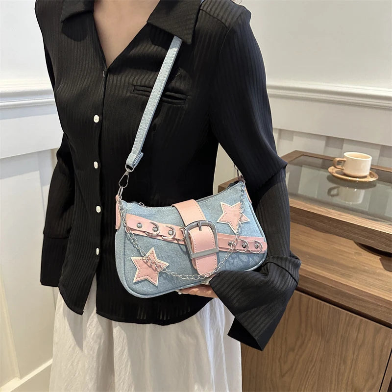 Person holding a denim handbag with star and belt design in an indoor setting.