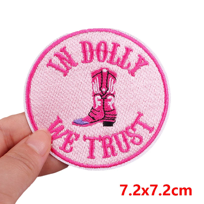 Embroidered patch with pink border and text held by a hand on a white background