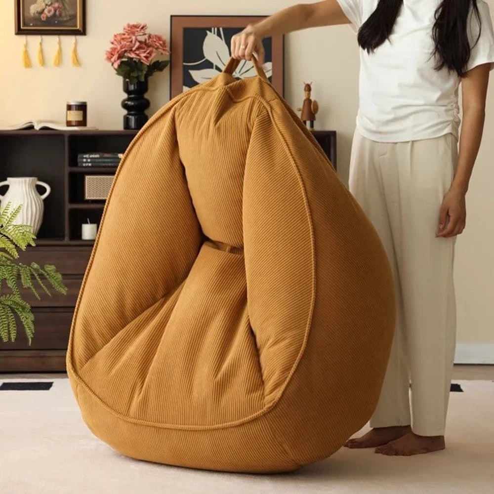 Person holding a mustard yellow bean bag chair in a room with decor elements.