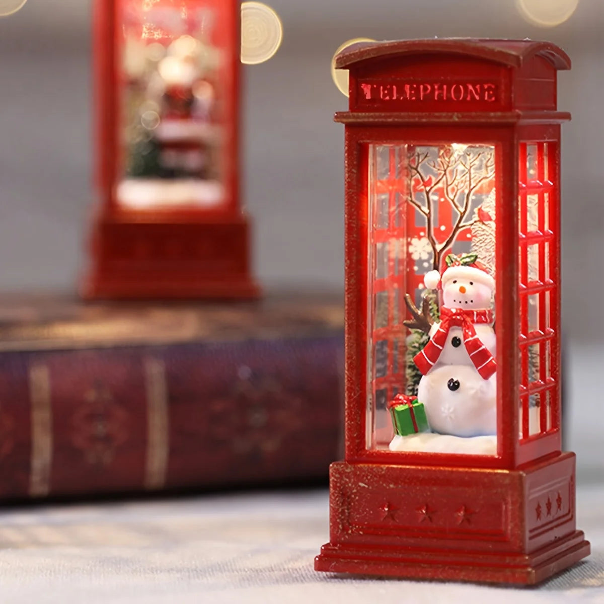 Decorative red telephone booth with a snowman inside, featuring a blurred background.