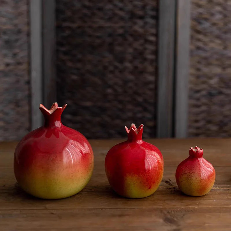 Three pomegranates of different sizes on a wooden surface with a textured wall background.