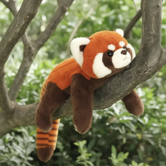 Plush toy red panda on a branch with green foliage in the background
