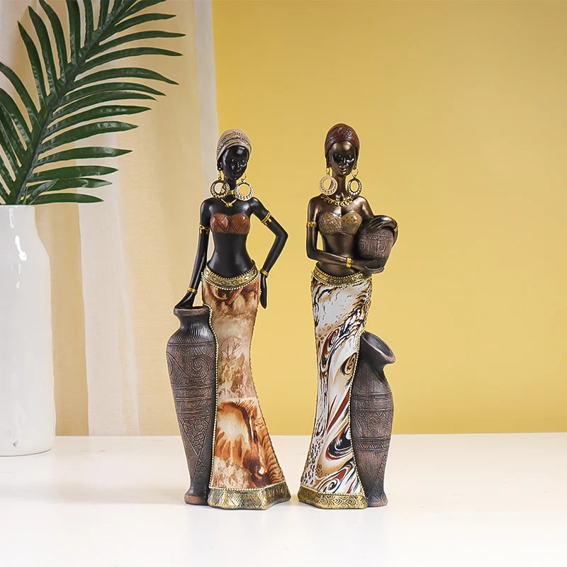 Two decorative statues of women holding vases on a white surface with a yellow wall background.