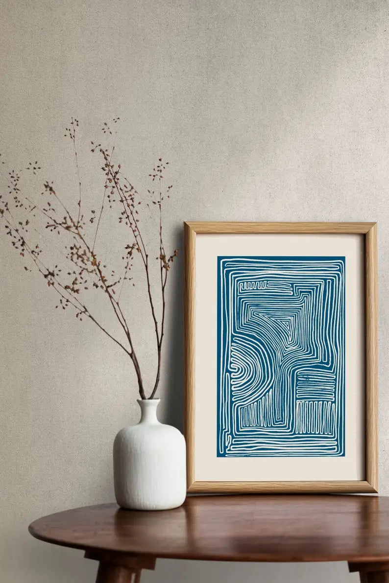 Framed abstract artwork on a wall next to a white vase with branches