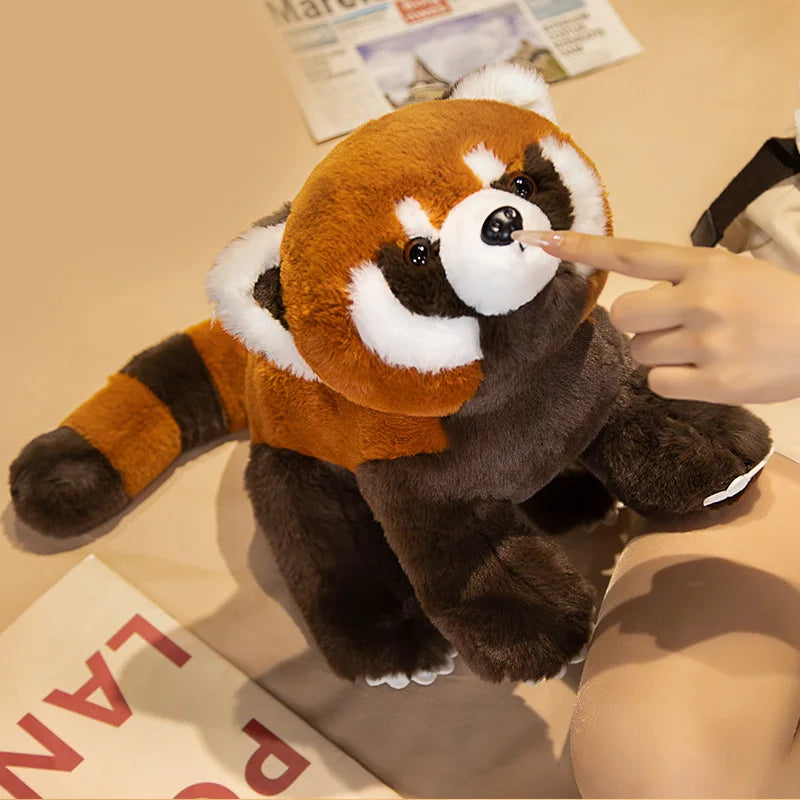 Plush toy red panda being held by a hand on a surface with newspaper in the background