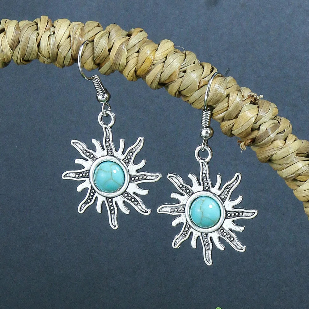 Sun-shaped earrings with turquoise stones on a straw background