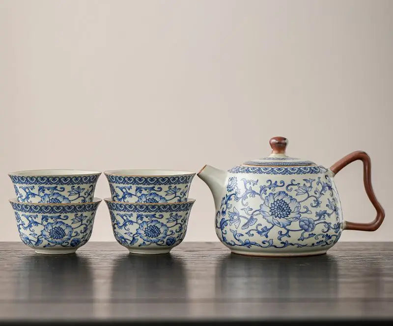 Ceramic teapot and cups with blue floral patterns on a wooden surface.