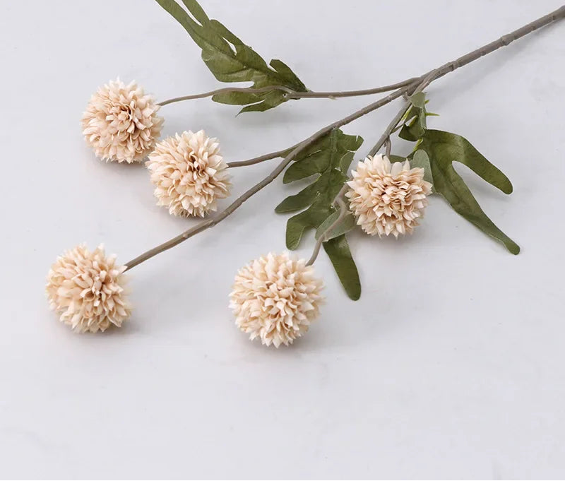Artificial flower branch with beige flowers and green leaves on a light gray background