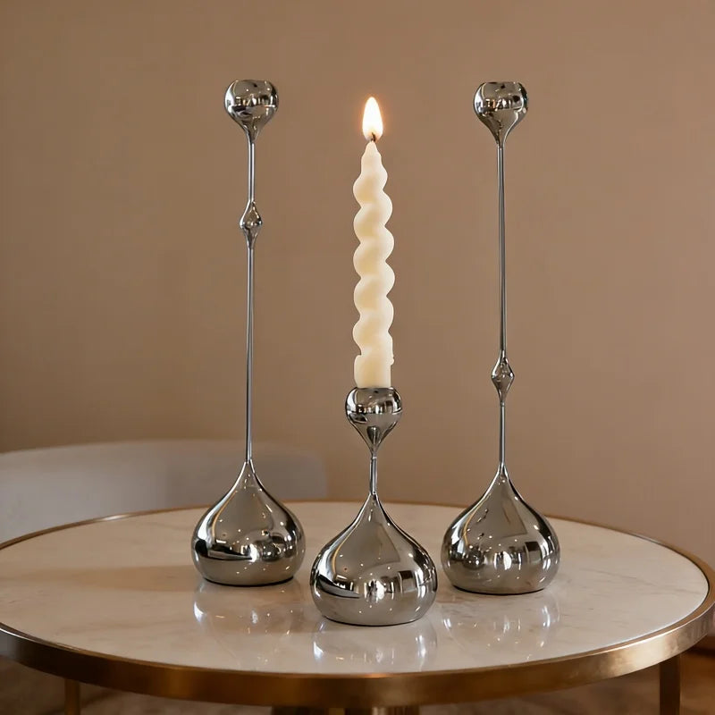 Three silver candle holders with a single white candle on a beige surface.