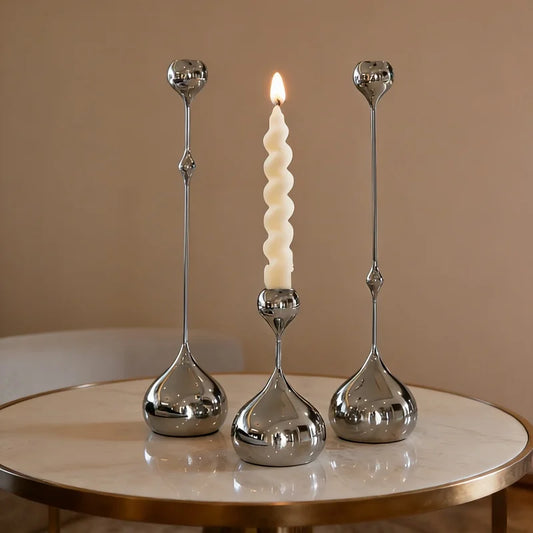 Three silver candle holders with a single white candle on a beige surface.