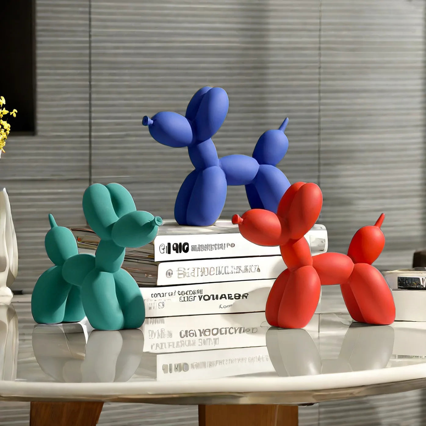 Three colorful balloon dog sculptures on a table with books in the background.