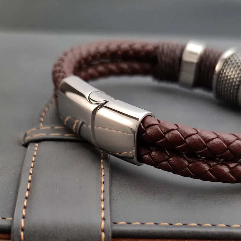 Brown braided leather bracelet with silver clasp on a gray textured surface