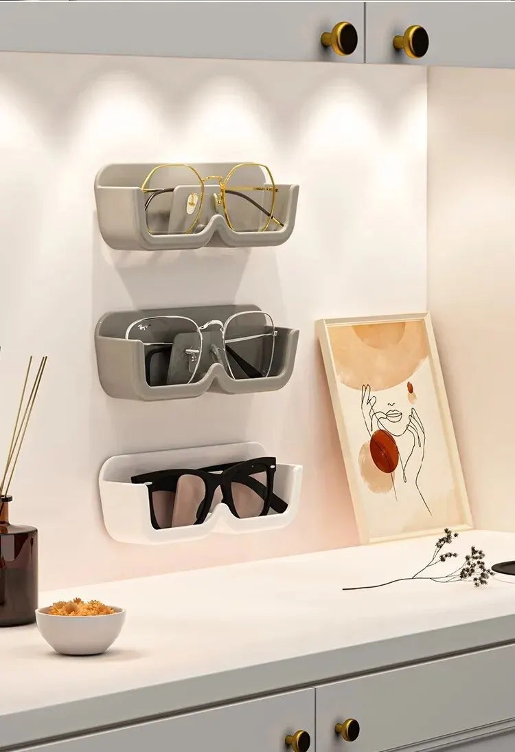 Wall-mounted sunglasses holder with glasses on a light-colored wall.