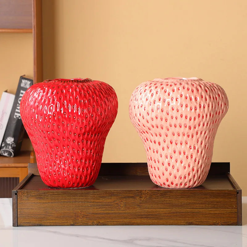 Two textured vases, one red and one pink, on a wooden stand against a beige wall.