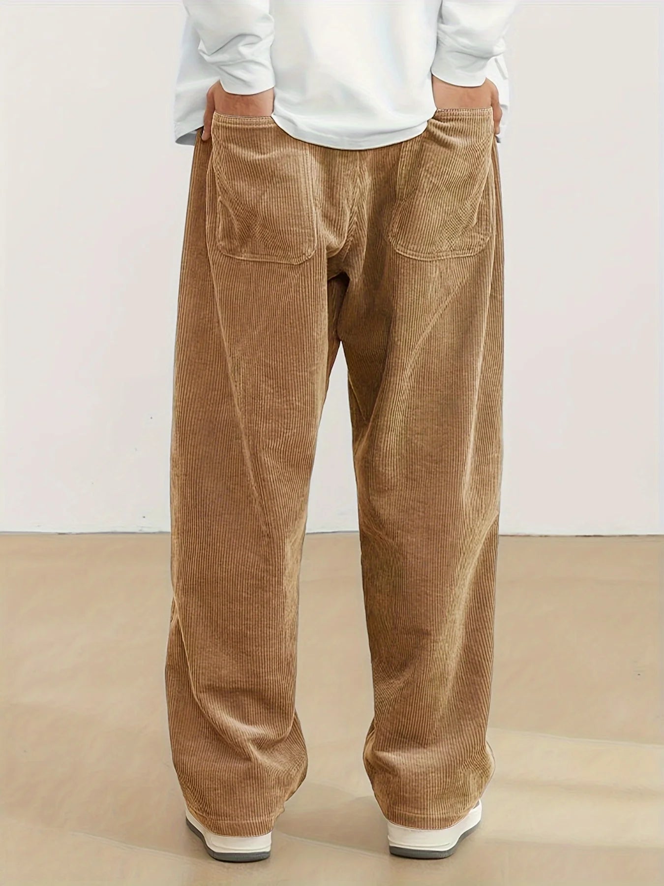 Person wearing brown corduroy pants and a white shirt on a beige background