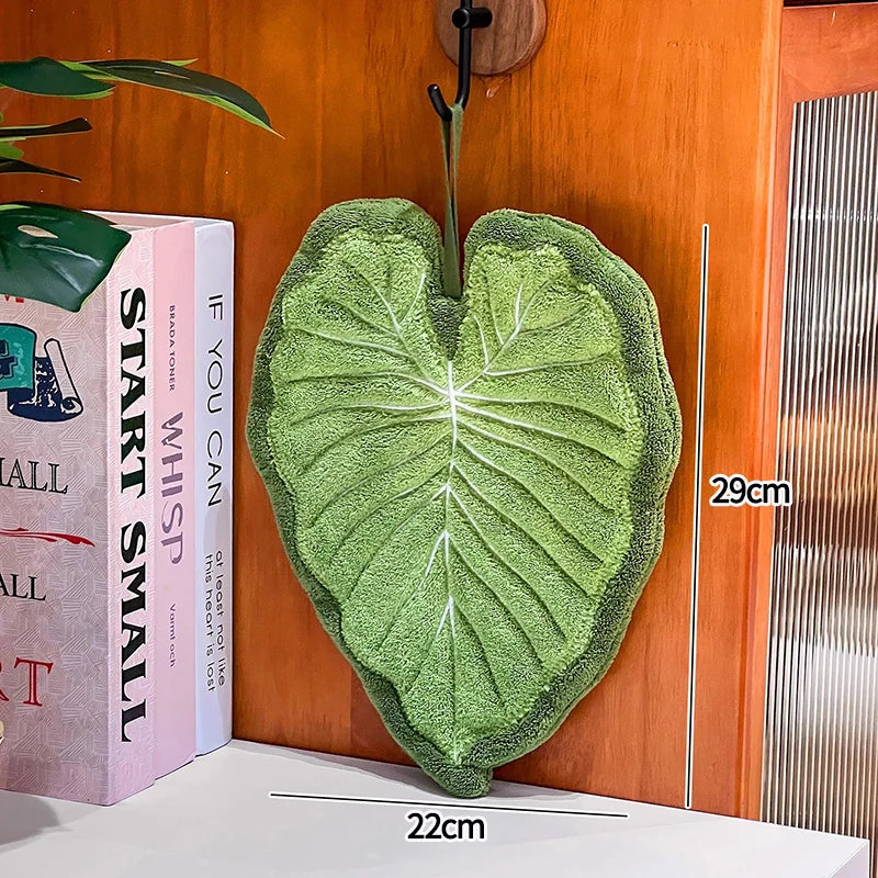 Green leaf-shaped towel on a wooden surface with books and a ruler for scale.