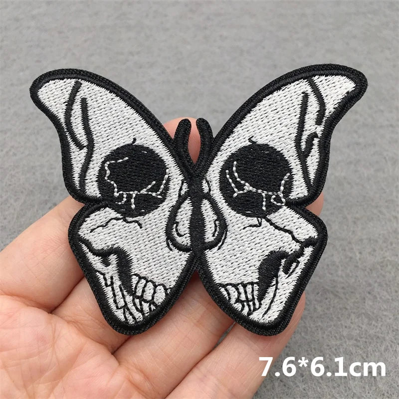Butterfly-shaped patch with skull design held in hand on a gray background