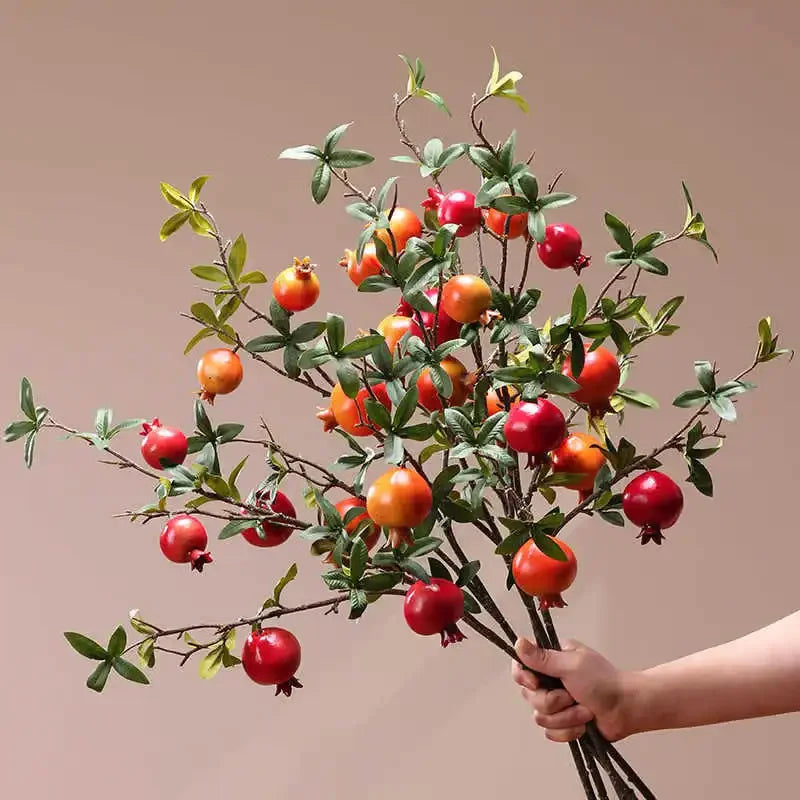 Bouquet of pomegranate branches held by a hand against a beige background