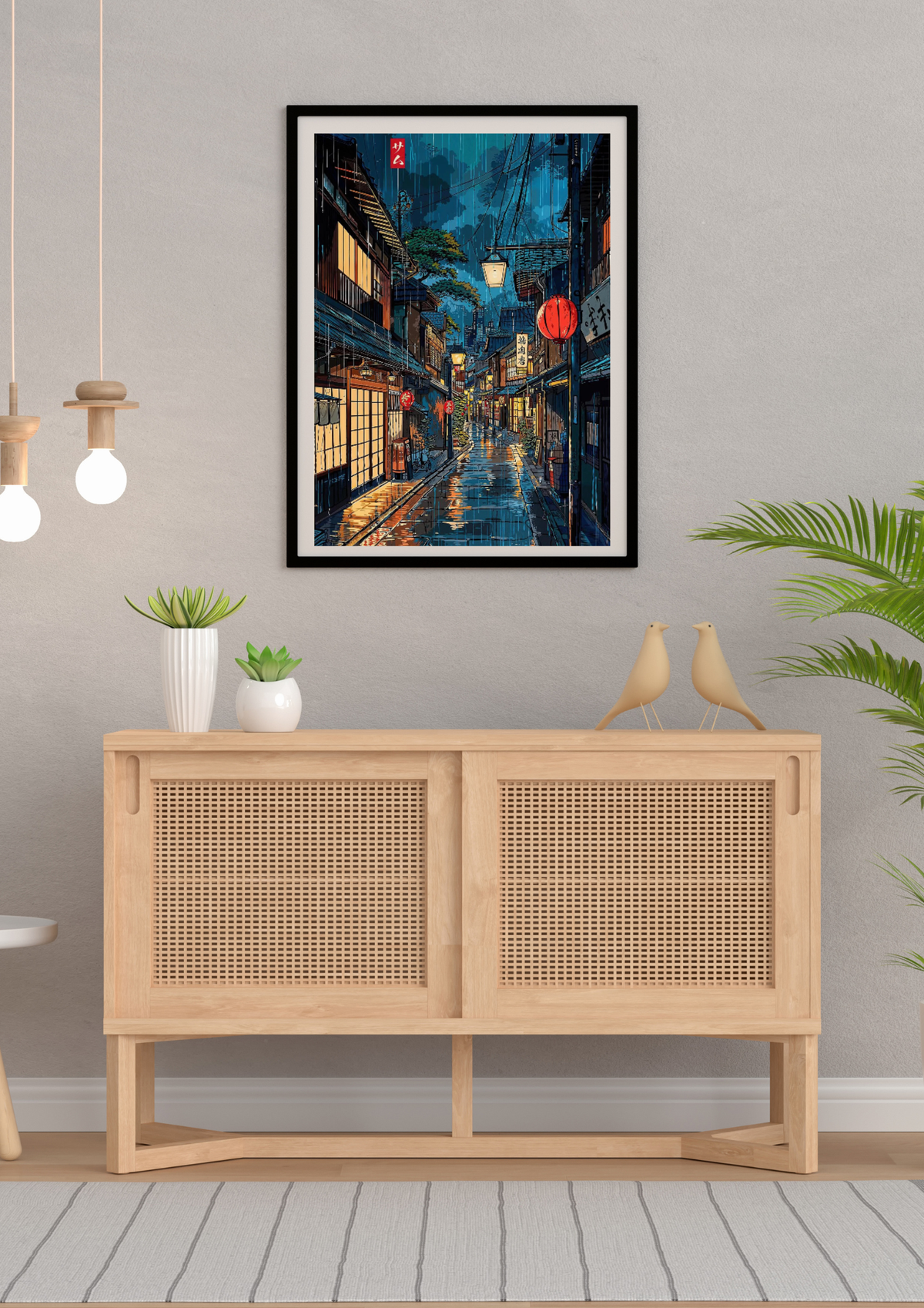 A framed vertical art print depicting a vibrant, colorful night street scene with lanterns and wet reflections, displayed on a light gray wall above a light wood sideboard in a styled room.