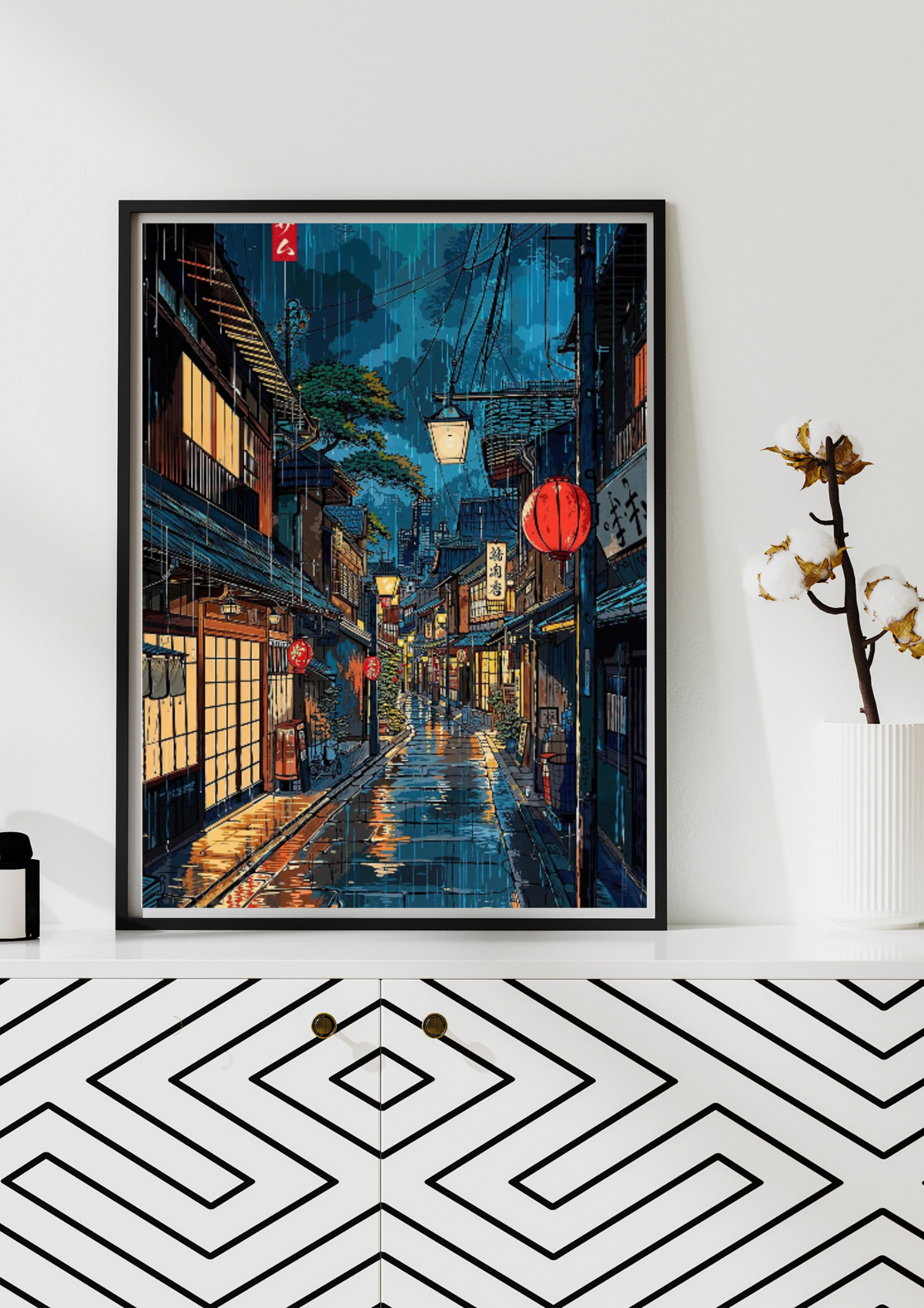 A framed vertical art print depicting a rainy Japanese street at night, styled on a white shelf above a black and white geometric patterned cabinet.