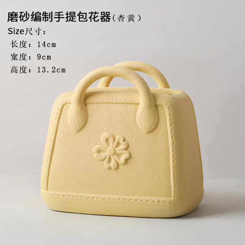 Yellow handbag-shaped flower pot with floral design on a light gray background