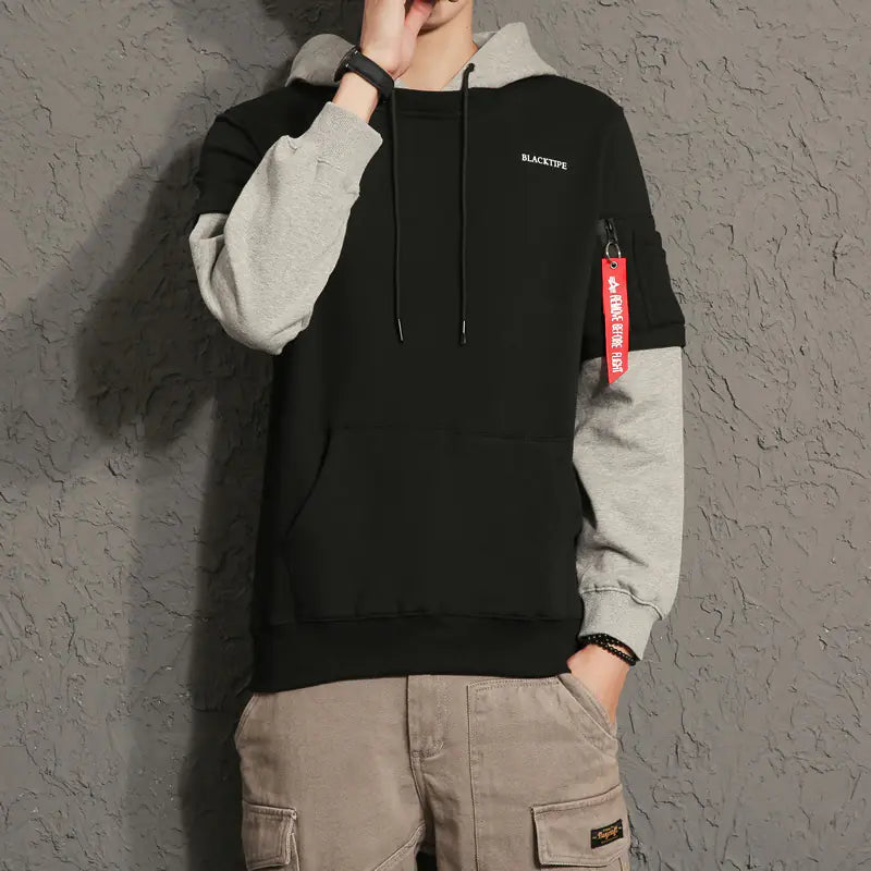 Person wearing a black and gray hoodie with a visible brand logo against a gray background