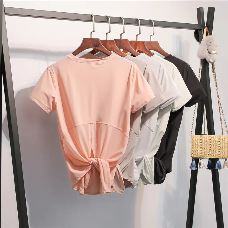 Three t-shirts in pink, white, and black hanging on a rack against a white background.