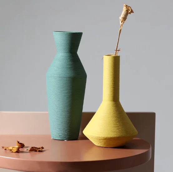Two ceramic vases, one green and one yellow, on a wooden surface with a gray background.