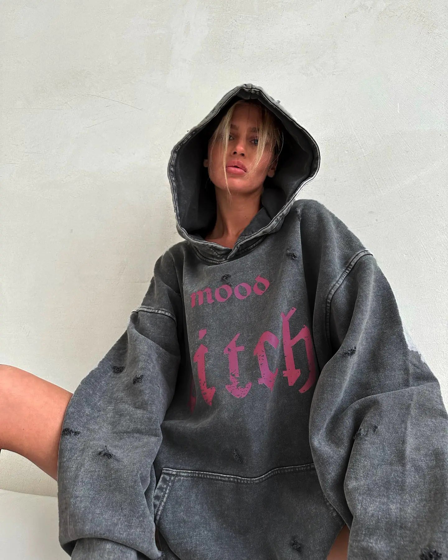 Person wearing a gray hoodie with pink text on a plain background