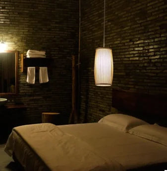 Dark bedroom with bed, lamp, and towels on a wooden stand.